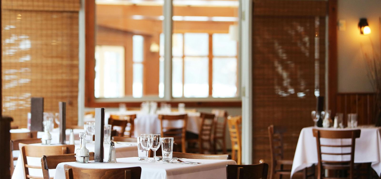 Empty tables set for dining in a restaurant with large windows.